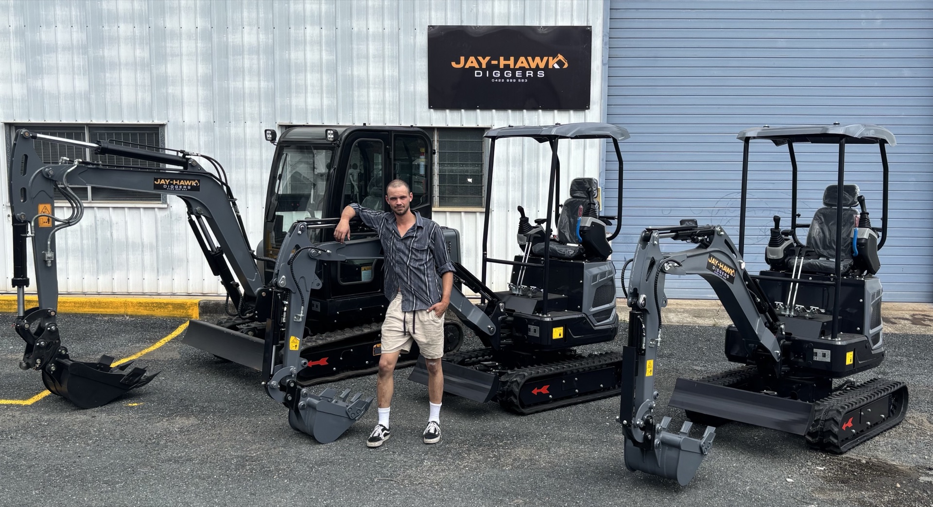 Jeremy Melhop in front of three Jay-Hawk Diggers mini excavators under the branded shop signage at Arana Hills